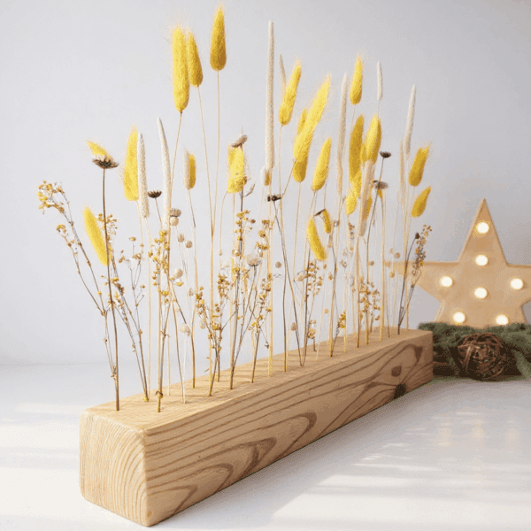 Centro de mesa boho con flores secas blancas y amarillas sobre barra de madera